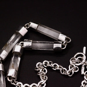 Handmade sterling silver and natural clear quartz crystal bar necklace coiled on black background, showing full length of crystal bar links transitioning into sterling silver belcher chain with T-bar toggle clasp, Thornhill Jewellery